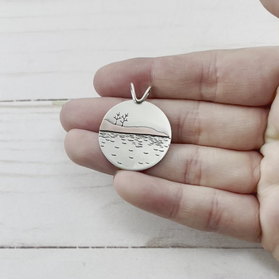 Round sterling silver pendant featuring hand sawn trees, a copper landscape and water details. Handmade by Beth Millner Jewelry. 