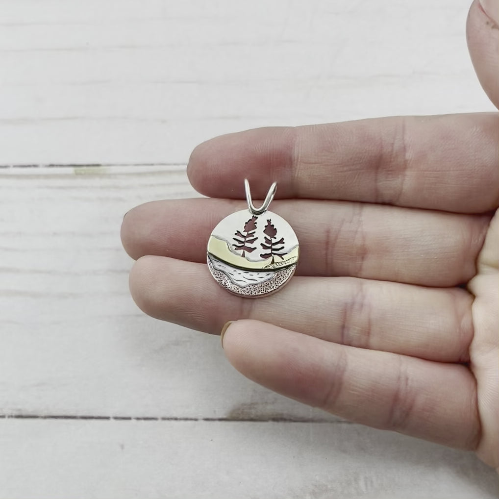 Round sterling silver pendant featuring hand sawn trees and copper and brass landscapes. Handmade by Beth Millner Jewelry.